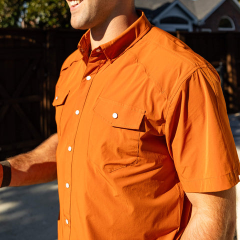 Man wearing an orange shirt outdoors with a blurred background
