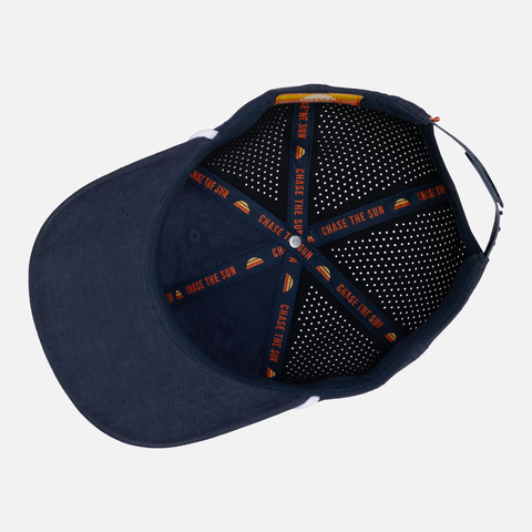 Inside view of Navy Performance Sueded Snapback showing interior taping with orange text "CHASE THE SUN"