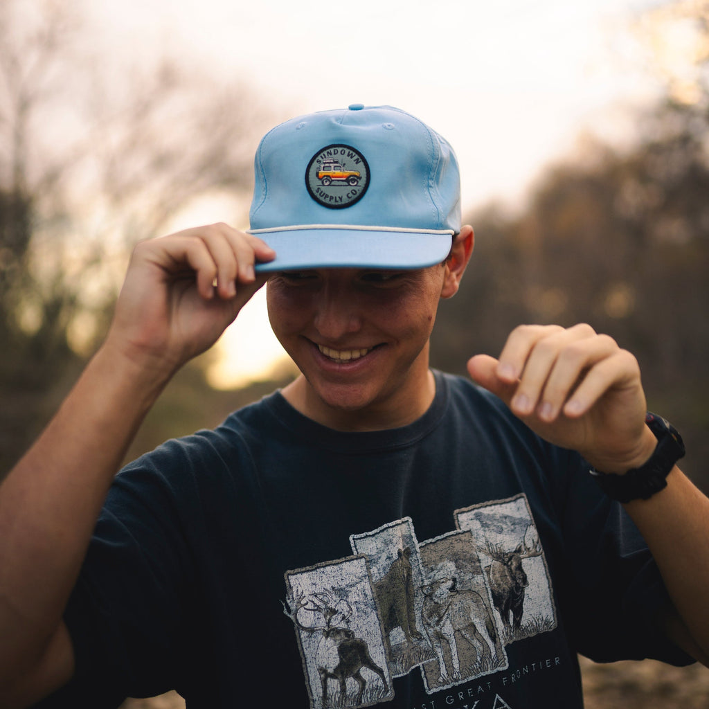 Person wearing a blue cap with a logo and a black t-shirt with graphic designs outdoors.