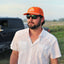 man standing in front of truck wearing white performance field shirt short sleeve and blaze sundown hat