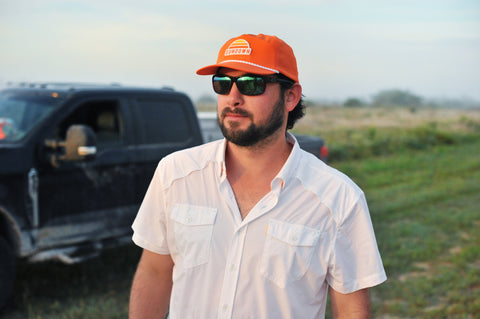 man standing in front of truck wearing white performance field shirt short sleeve and blaze sundown hat