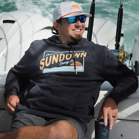 Man wearing a Sundown Supply Co hoodie and cap on a boat