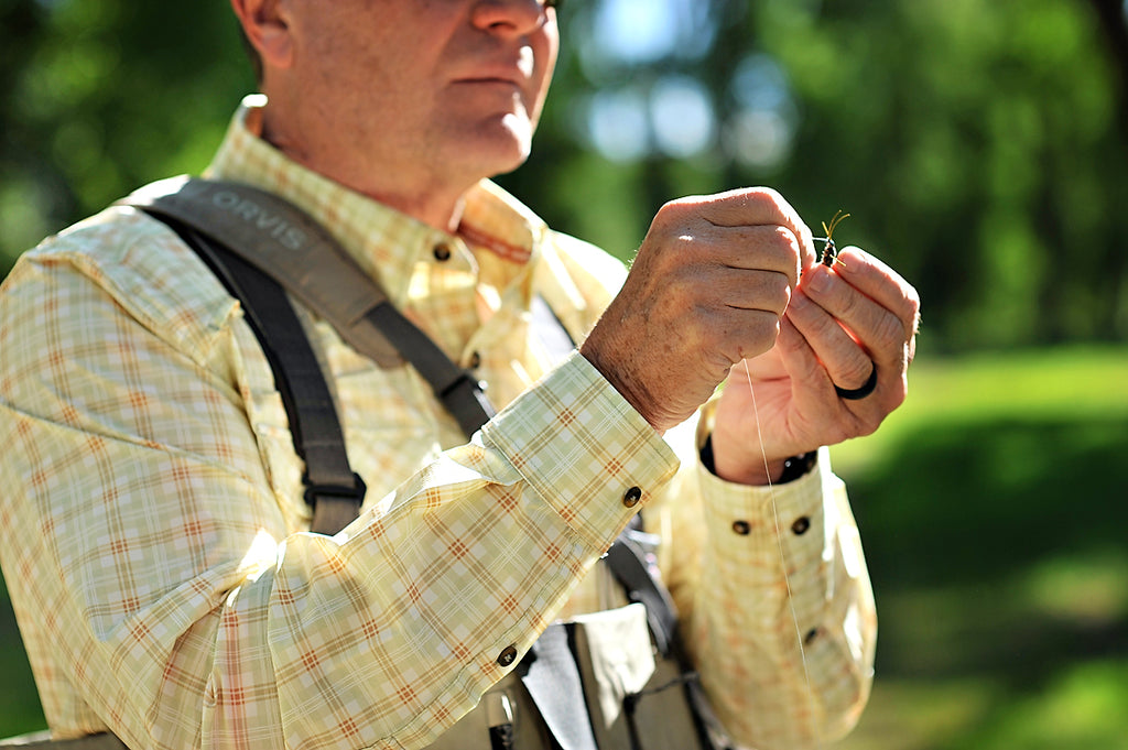 Man holding a fishing fly with a blurred green background