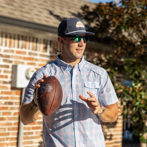 Man holding a football outdoors with a building and tree in the background