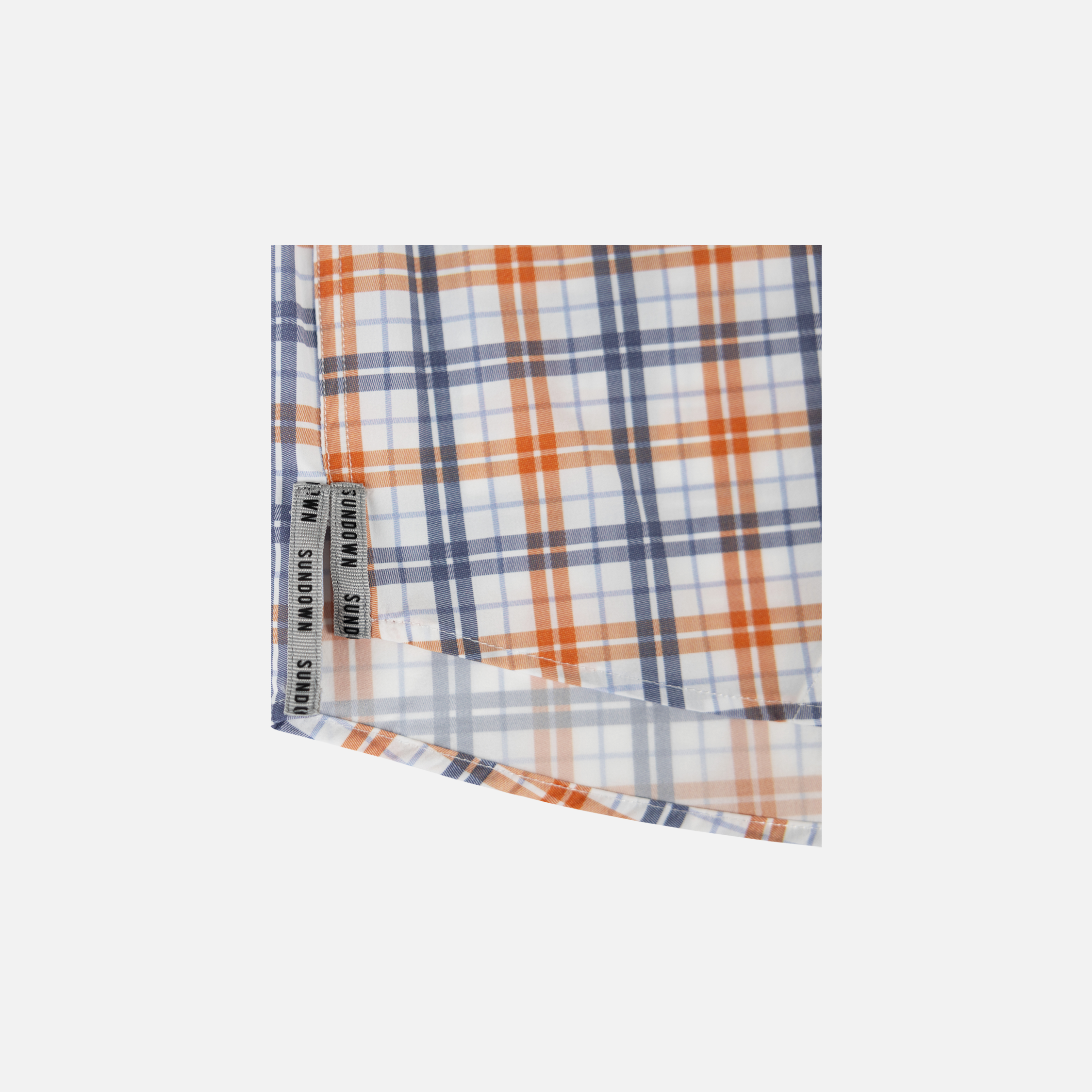 Closeup of bottom side edge of Orange/Navy Plaid Pearl Snap Field Shirt L/S showing grey side slits with black "SUNDOWN" text - Sundown Supply Co