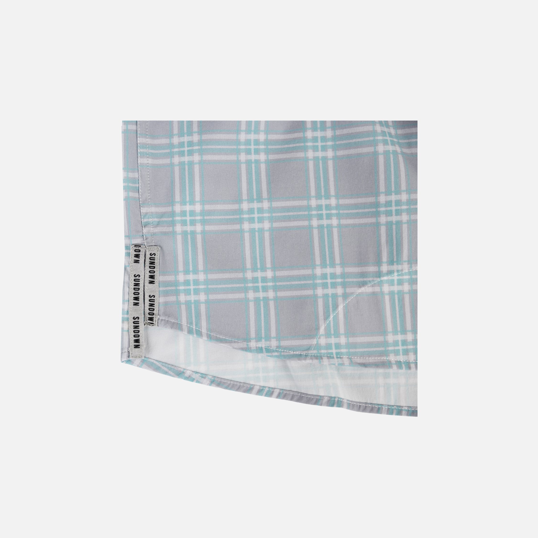 Closeup of bottom side edge of Seafoam/Grey Plaid Pearl Snap Field Shirt L/S showing grey side slits with black "SUNDOWN" text - Sundown Supply Co