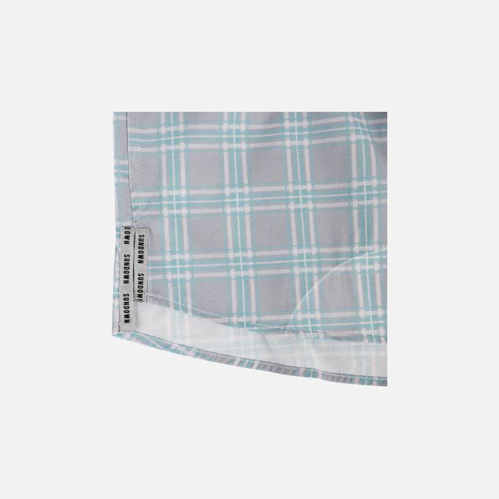 Closeup of bottom side edge of Seafoam/Grey Plaid Pearl Snap Field Shirt S/S showing grey side slits with black "SUNDOWN" text
